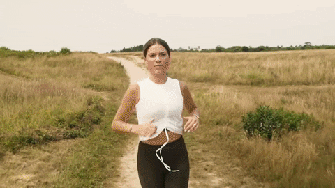 Person jogging on a dirt path through a grassy field.