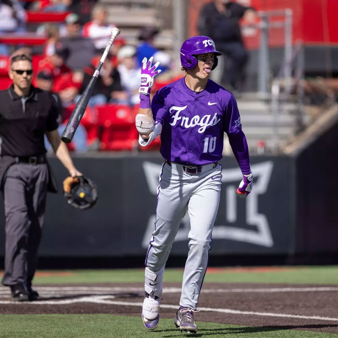 Baseball player in purple uniform celebrates, bat in air, umpire in background.