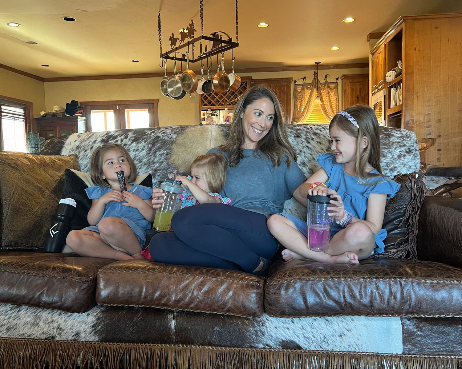 A woman sitting on a couch with three children holding drinks.