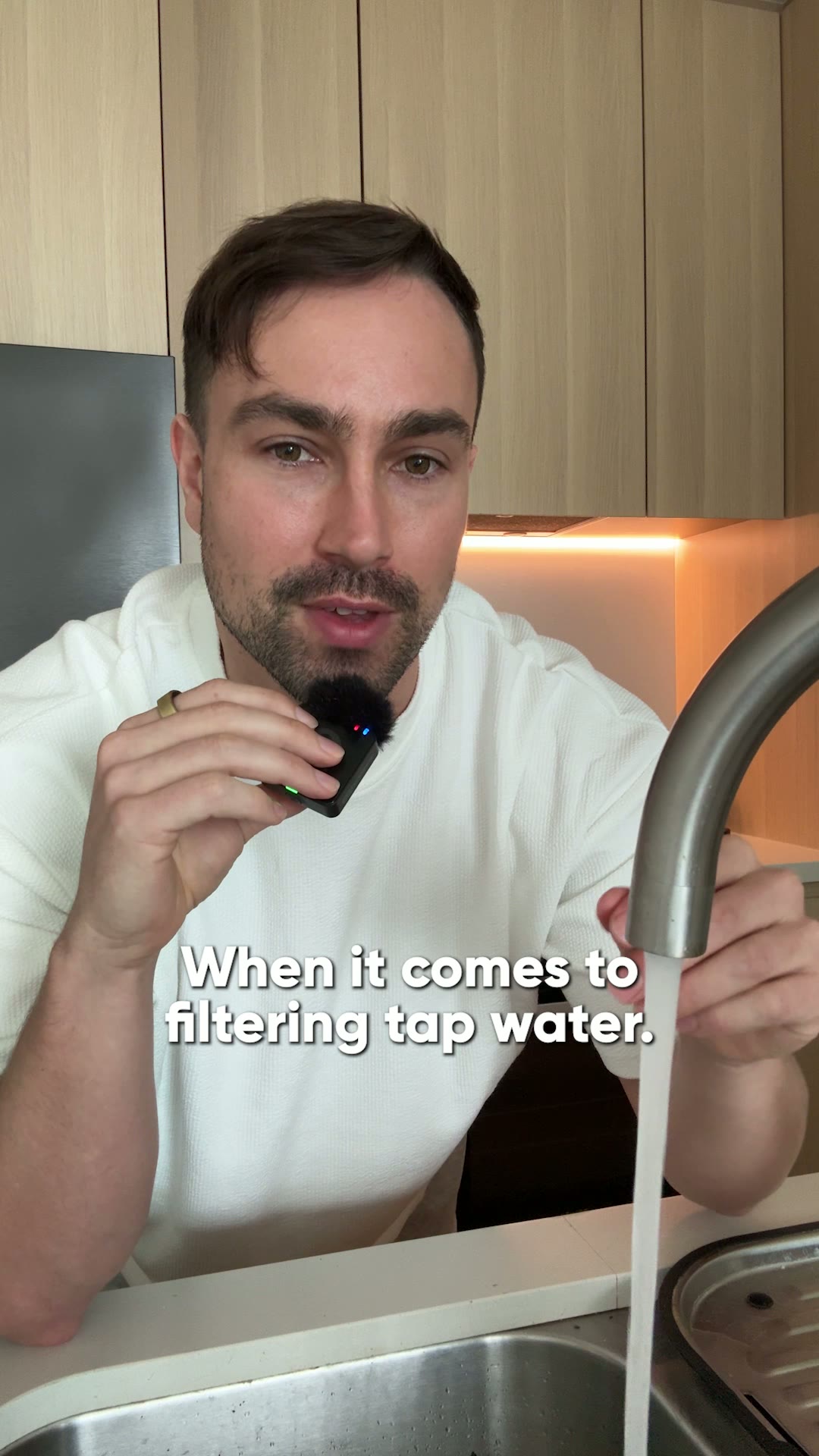 Person holding a microphone near a running kitchen faucet.