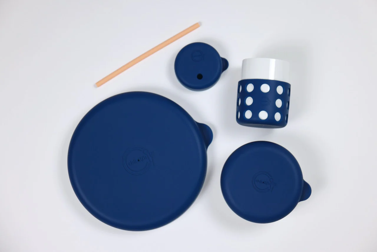 A blue polka-dotted cup, three matching blue silicone lids, and a straw on a white background.