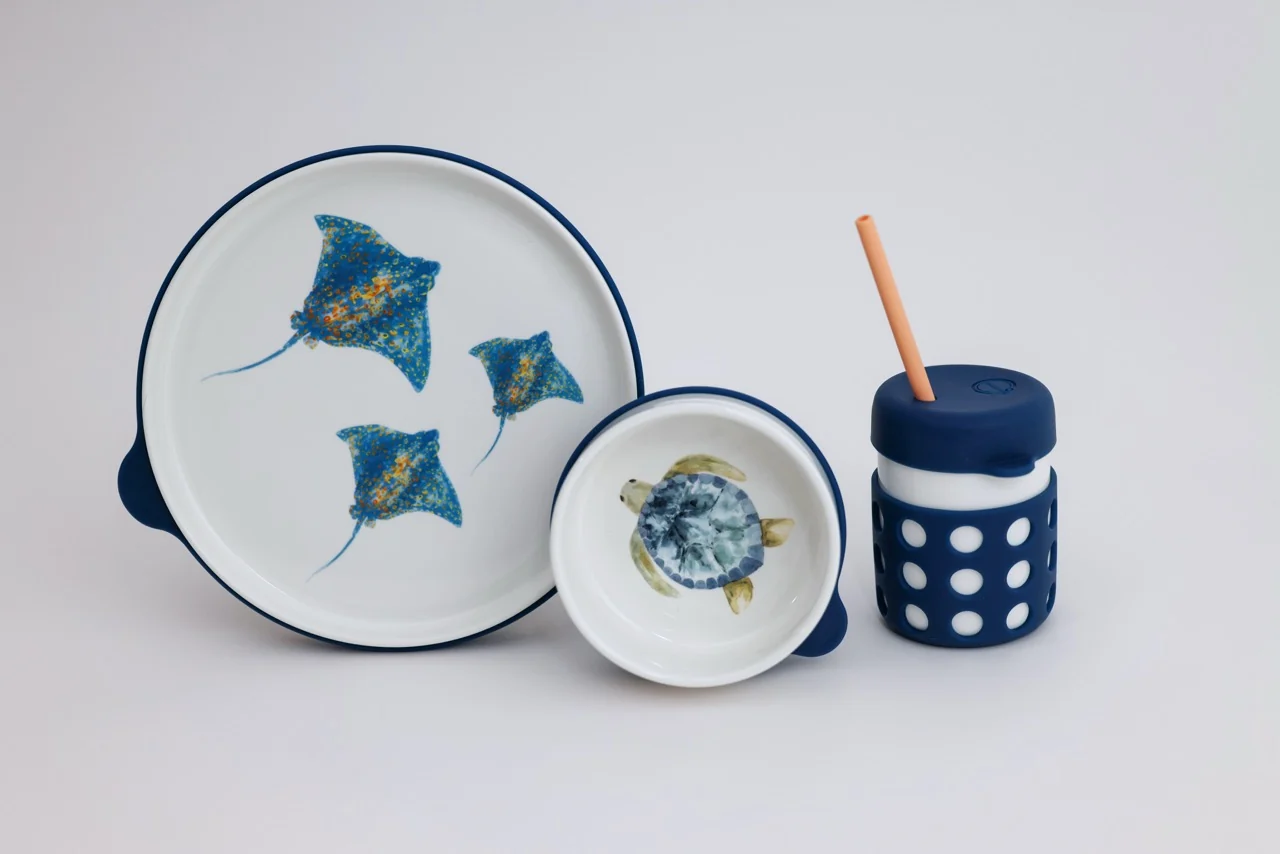 A children's dishware set with a plate, bowl, and cup, decorated with stingrays and a sea turtle.