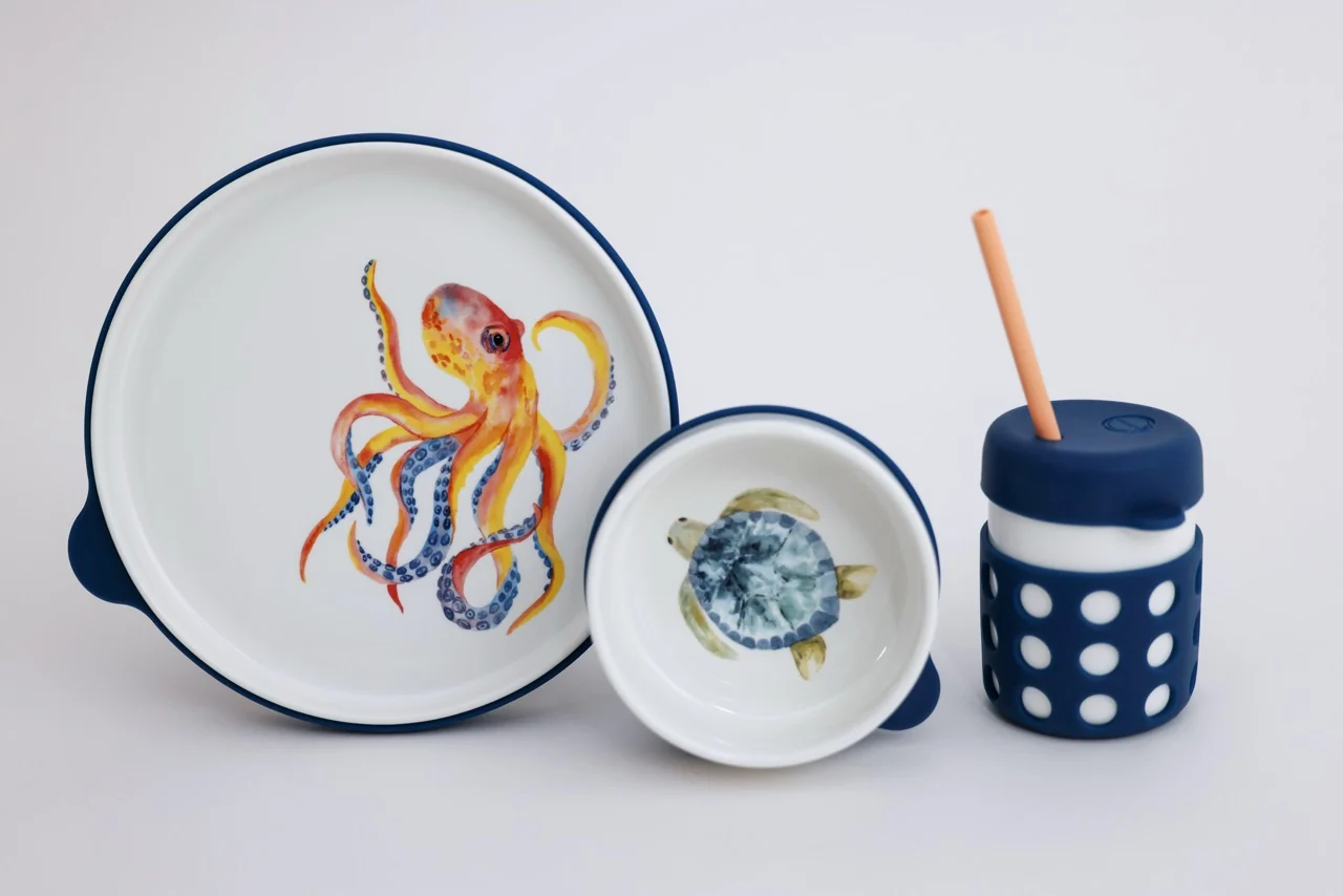 A children's dining set with an octopus plate, a turtle bowl, and a cup with a straw.