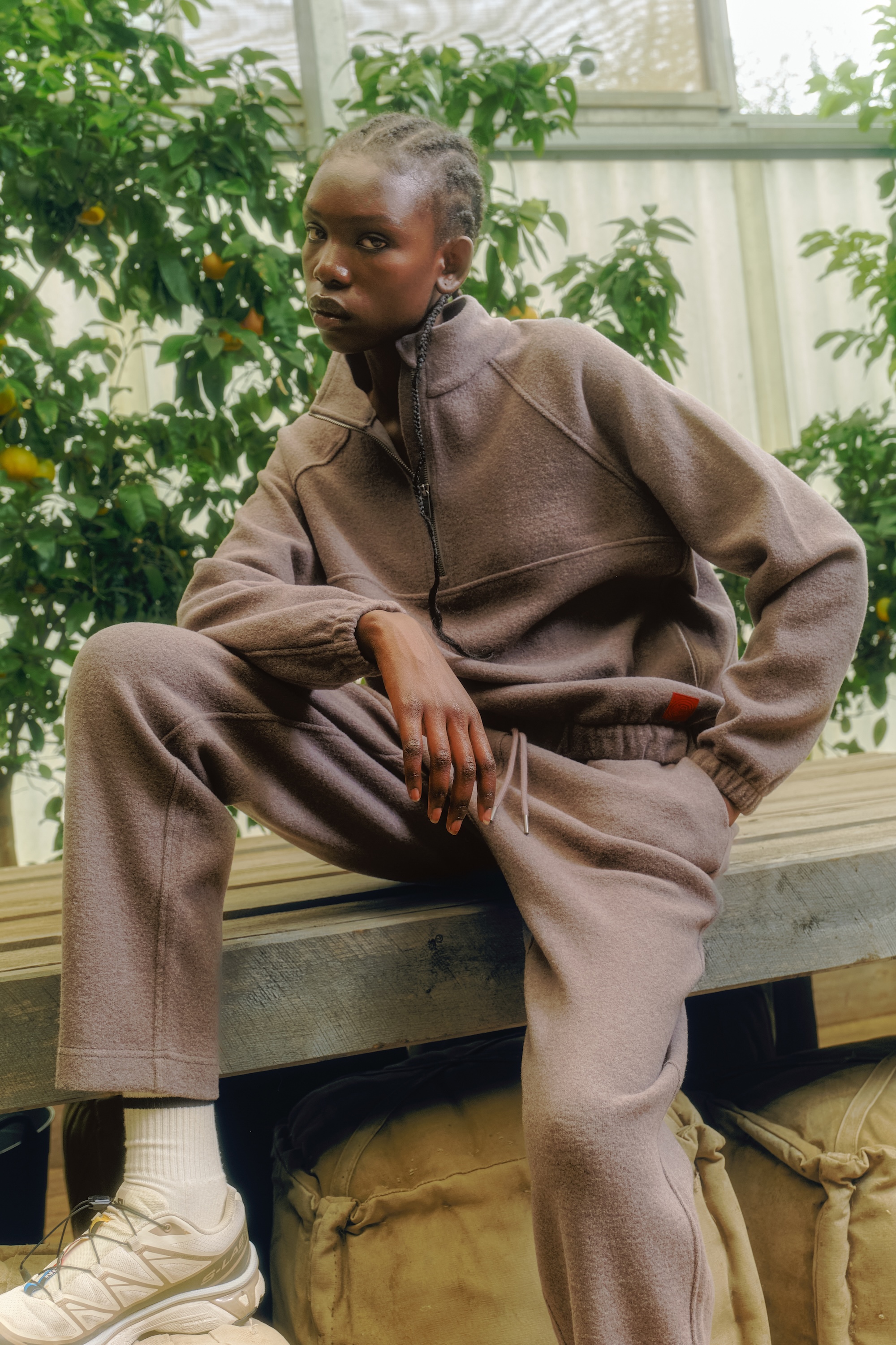 Person in cozy tracksuit sitting on a wooden platform, surrounded by greenery.
