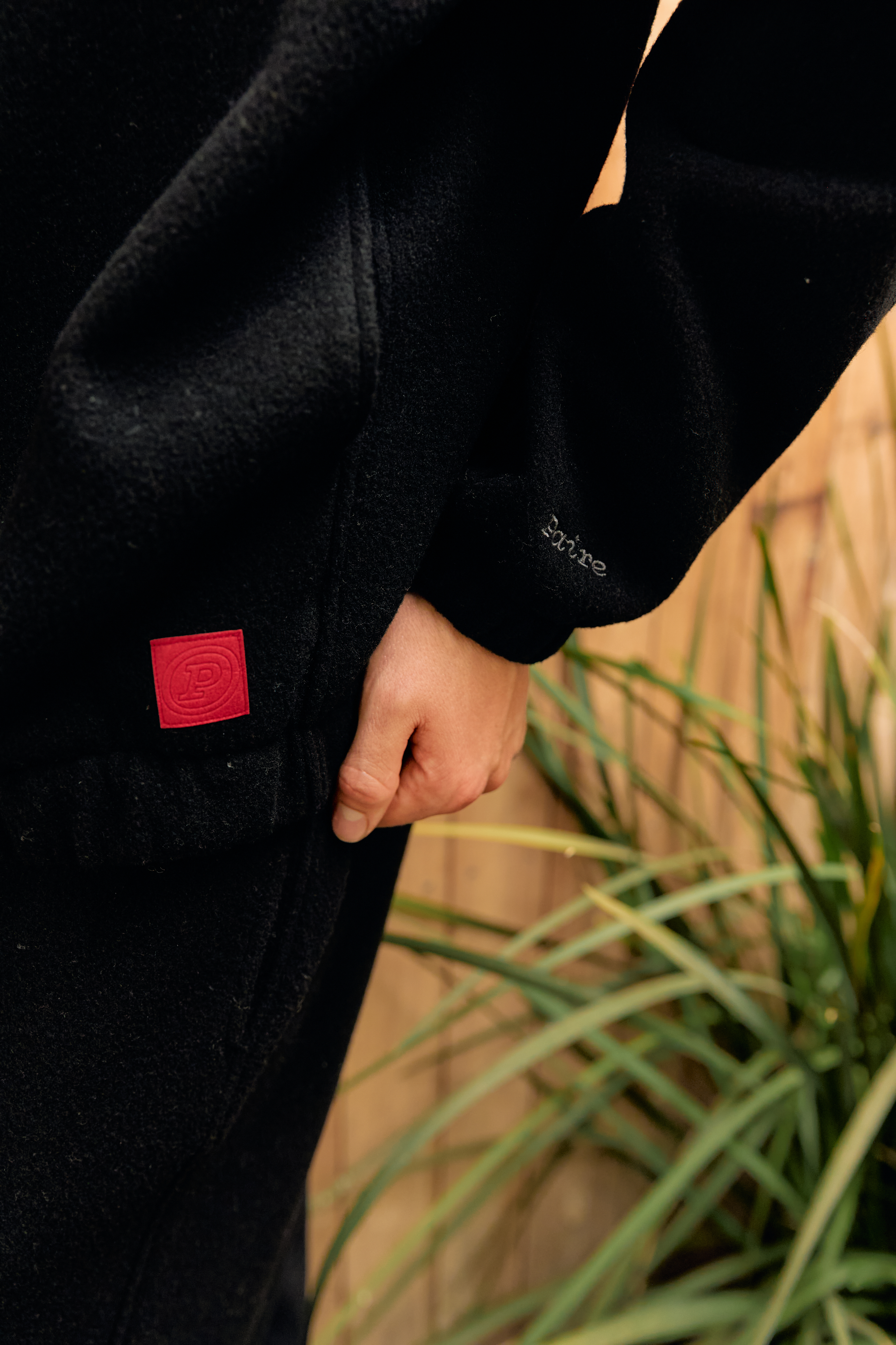 Person in black fleece with red tag, standing near plants.