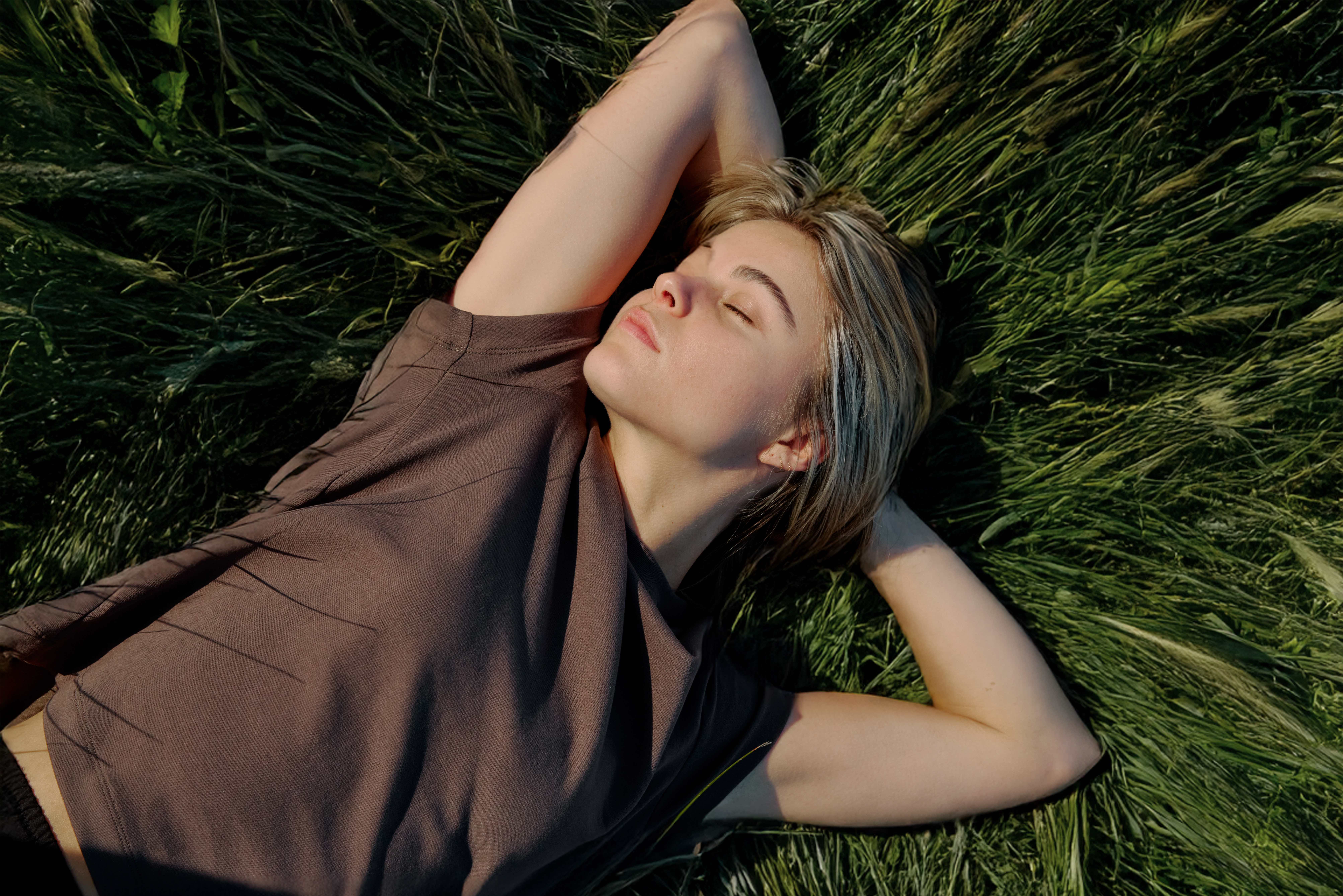 Person lying in green grass with eyes closed, arms behind head.