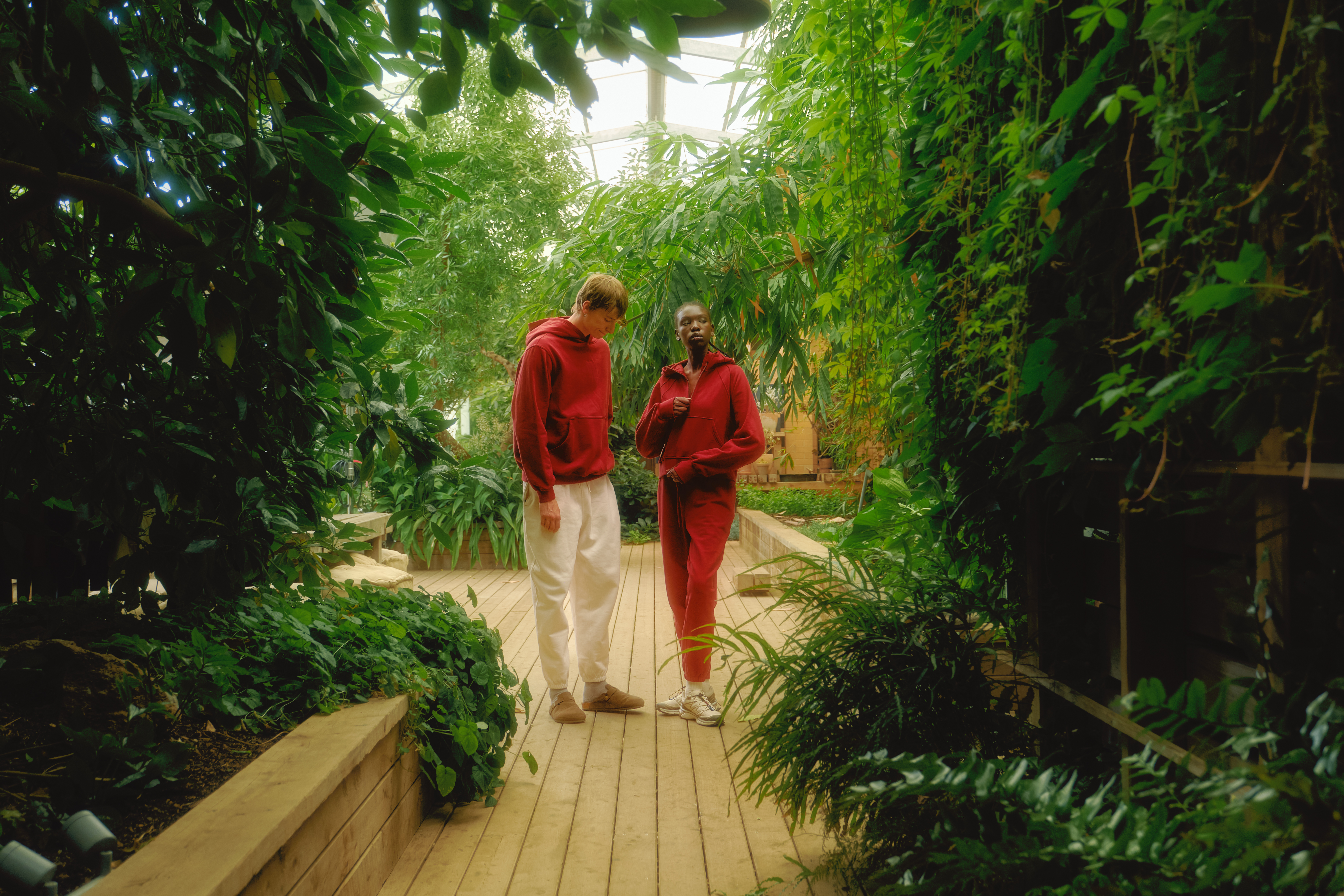 Two people in red outfits walking through a lush, plant-filled indoor garden.