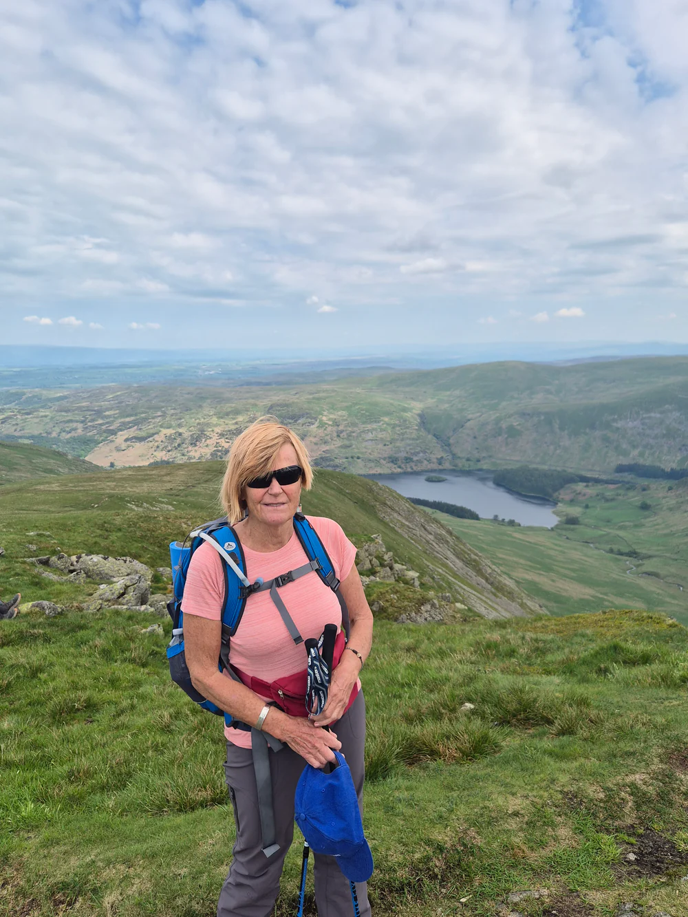 Woman hiking on a grassy hilltop with a scenic landscape view.