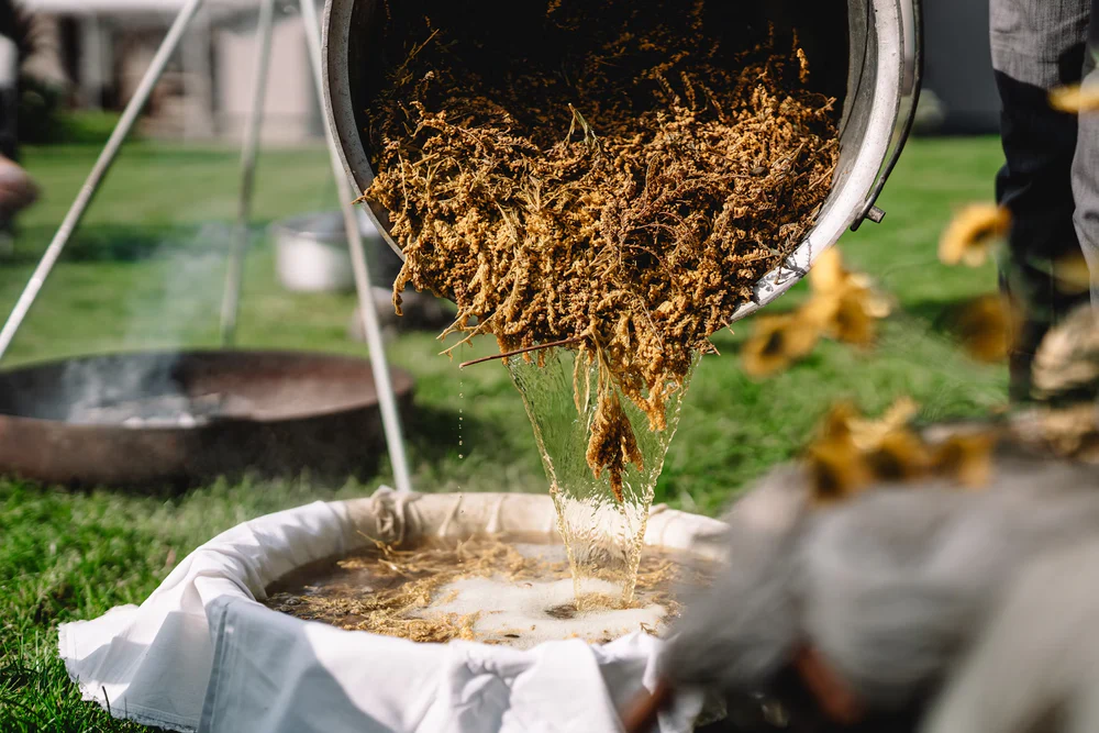 Pouring hot liquid and grains into a cloth-lined container outdoors.