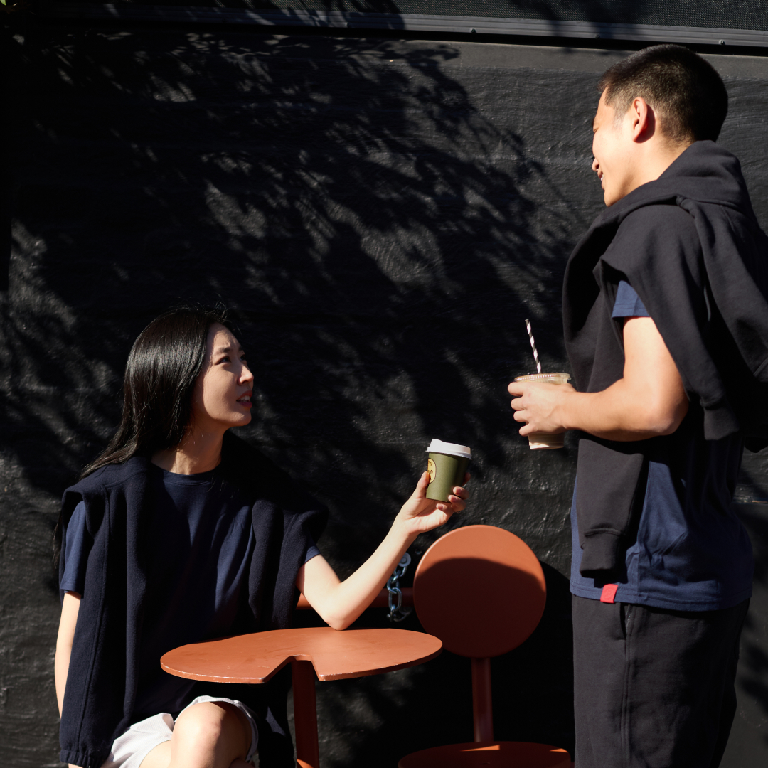 Two people sharing drinks at an outdoor café table, cast in shadow.
