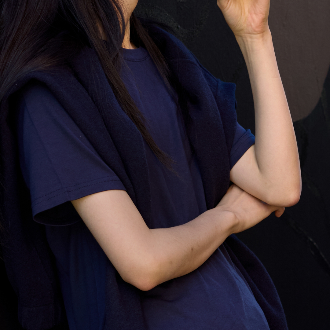 Person in a blue shirt with arms crossed and hand raised.