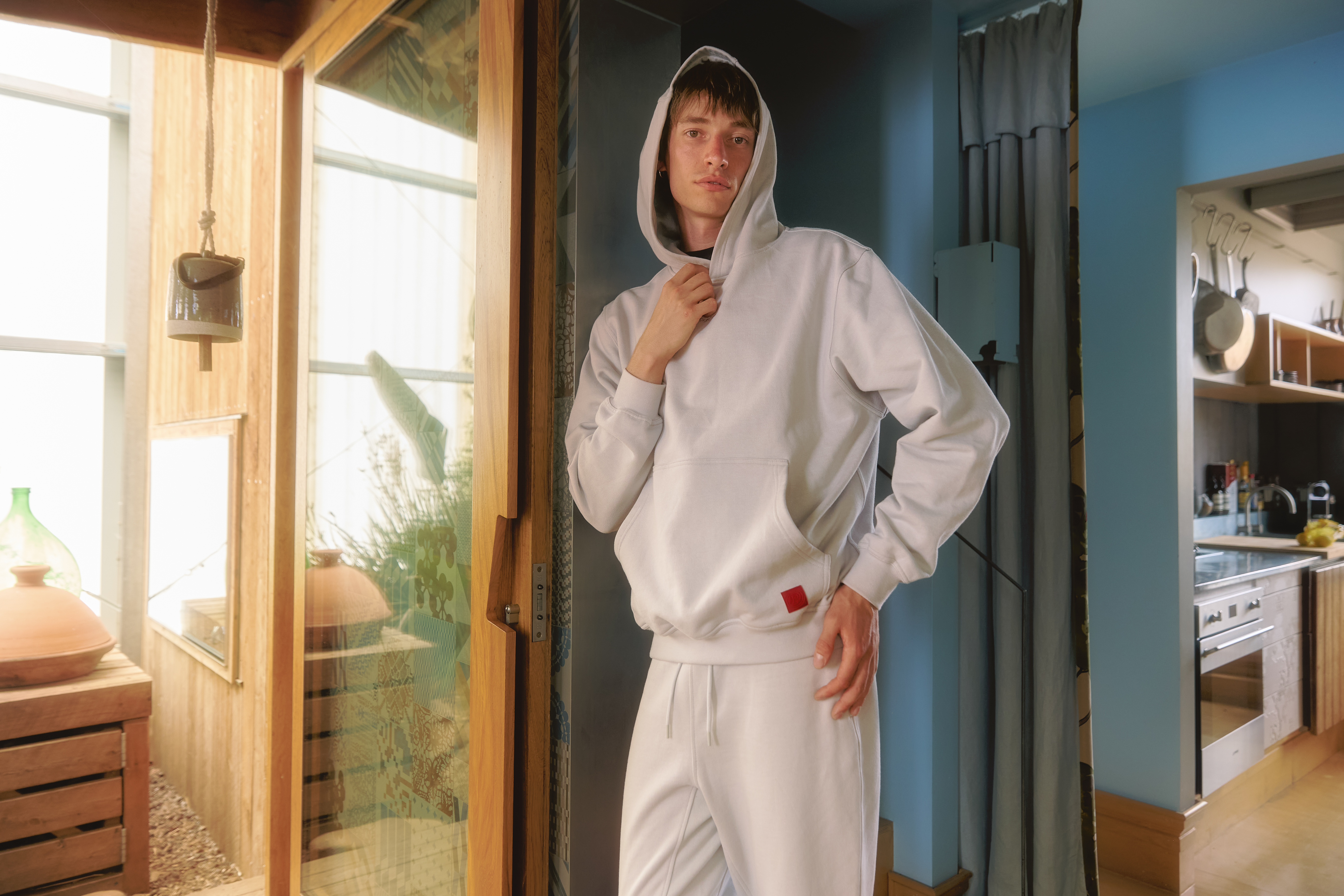 Person in a white hoodie and sweatpants, standing near a wooden door indoors.