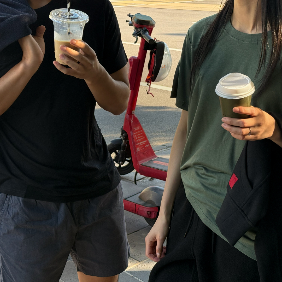 Two people holding drinks, standing near a red scooter.