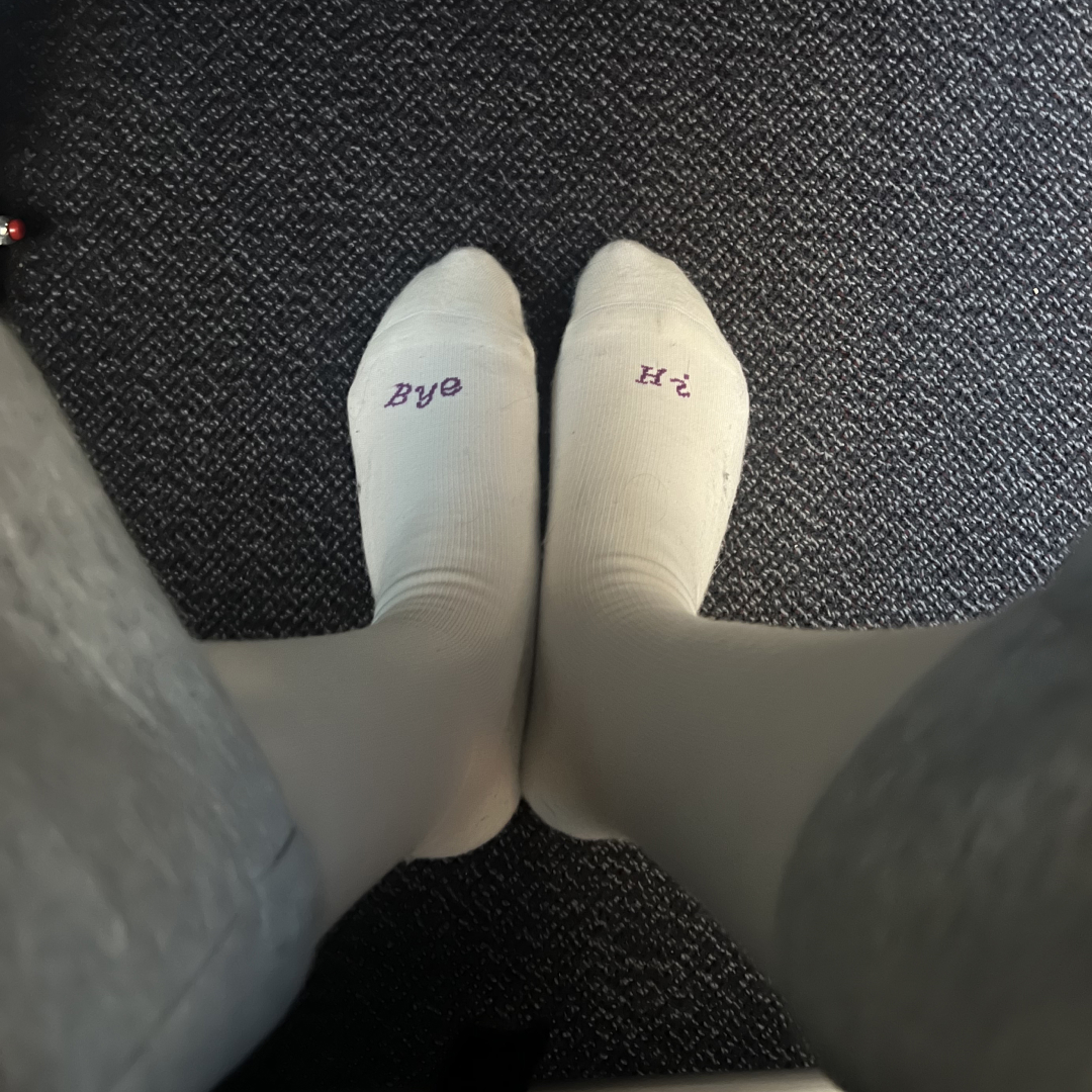 Feet wearing socks with 'Hi' and 'Bye' written on them.