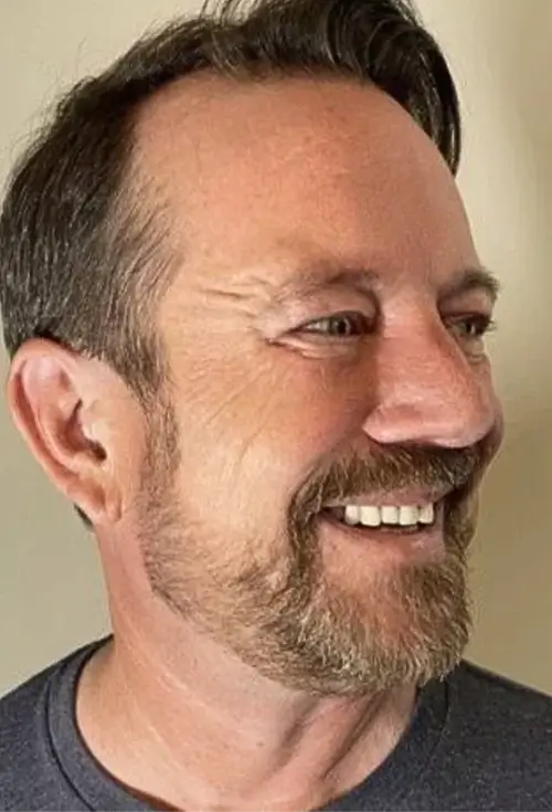 Man with a beard smiling and looking to the side.