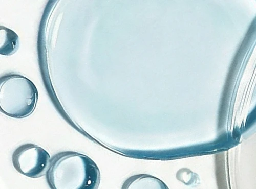A close-up of light blue liquid drops and a larger puddle on a white surface.
