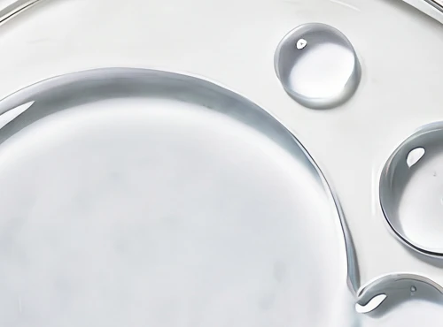 A close-up abstract image of clear liquid drops and swirls on a white surface.