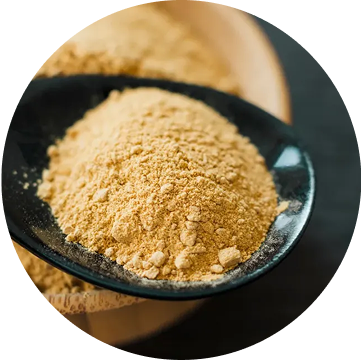 A black spoon filled with light brown powder on a wooden surface.