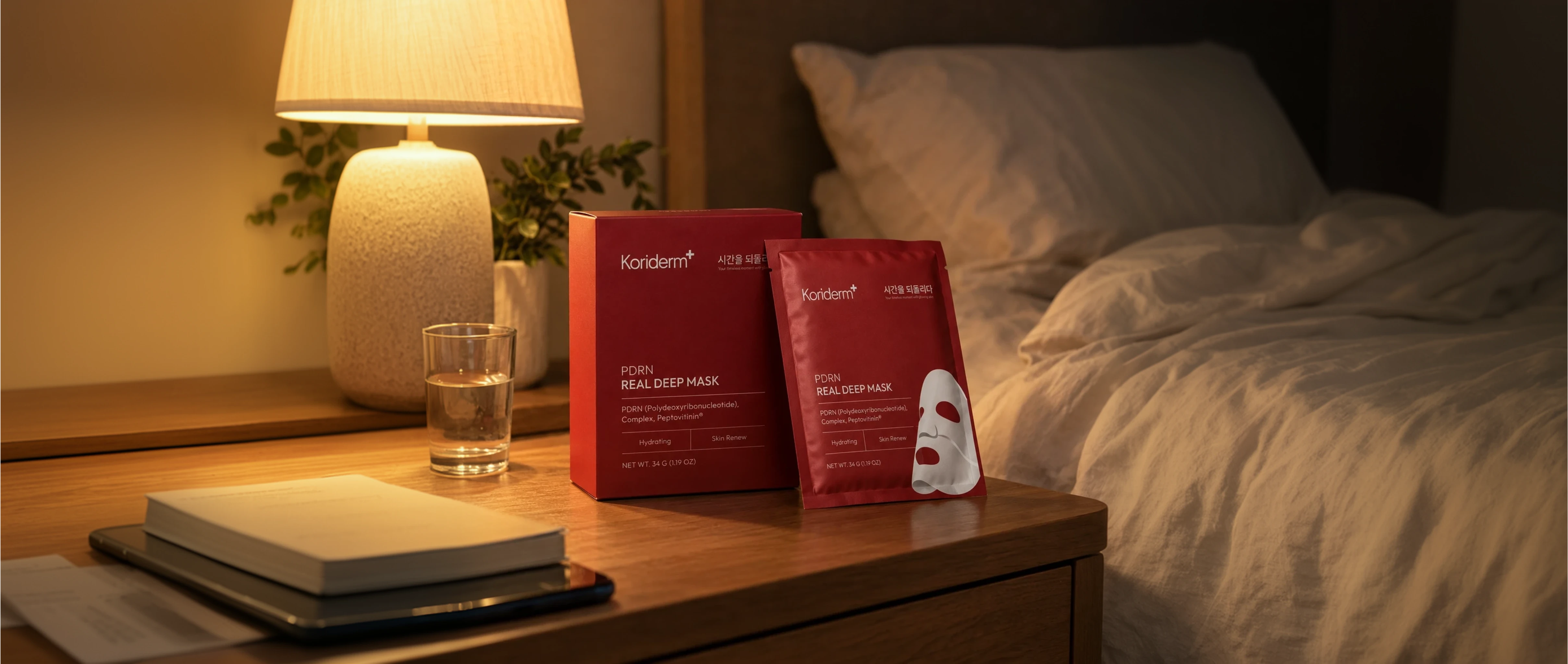 Koriderm face mask box and packet on a bedside table next to a lamp and bed at night.
