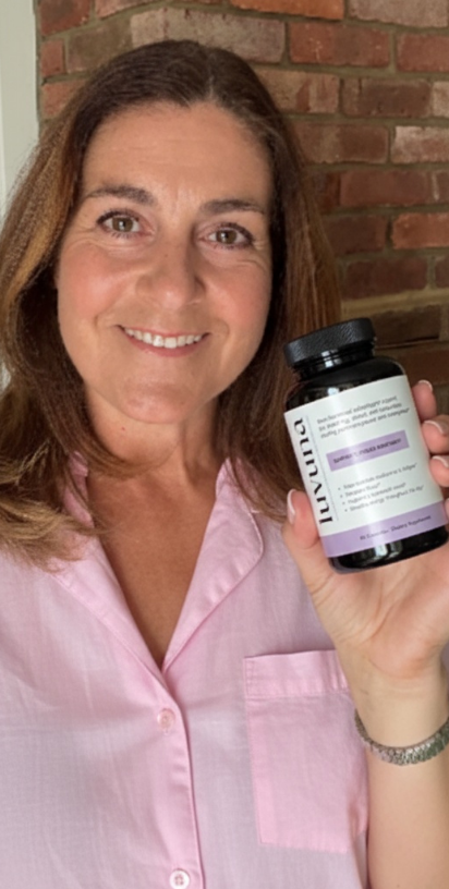 Person smiling holding a bottle against a brick wall background.