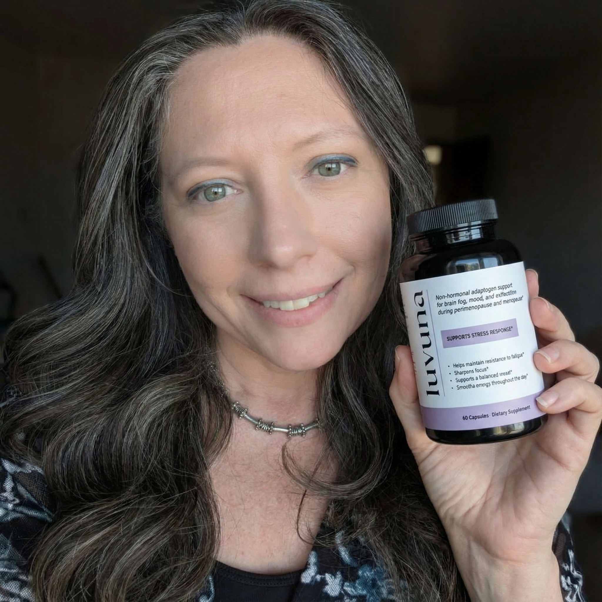 Person holding a bottle labeled 'luvuna' dietary supplement, smiling.