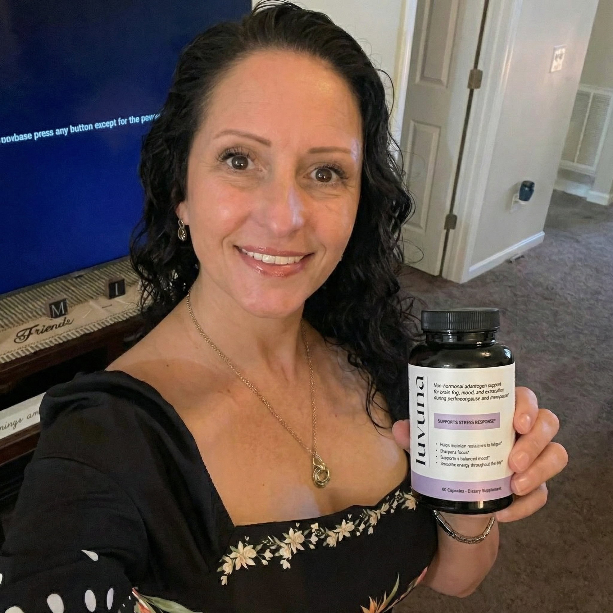 Person holding a bottle labeled 'Luvuna' in a room with a TV in the background.