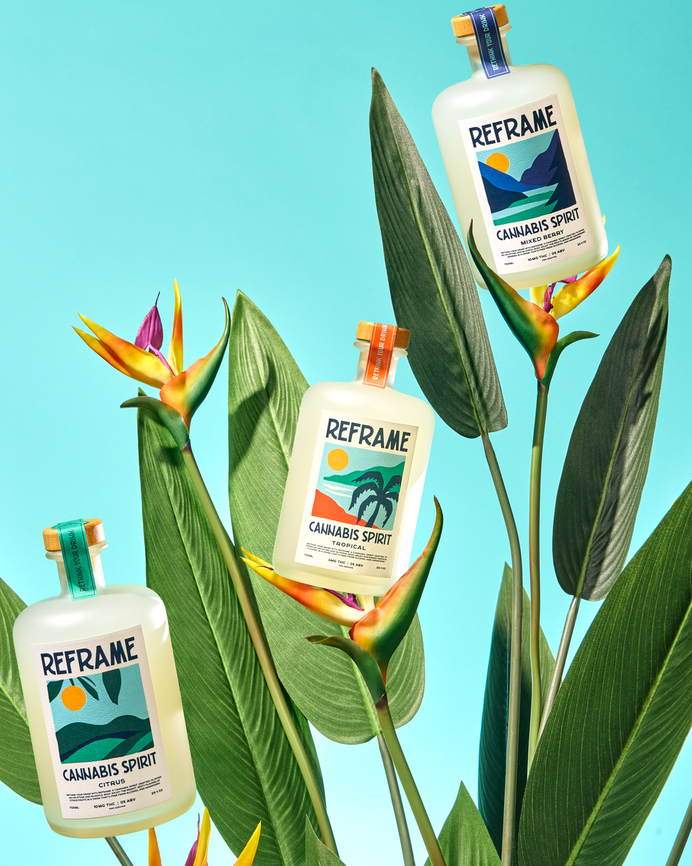 Three bottles labeled 'Reframe Cannabis Spirit' among tropical leaves and flowers on a turquoise background.