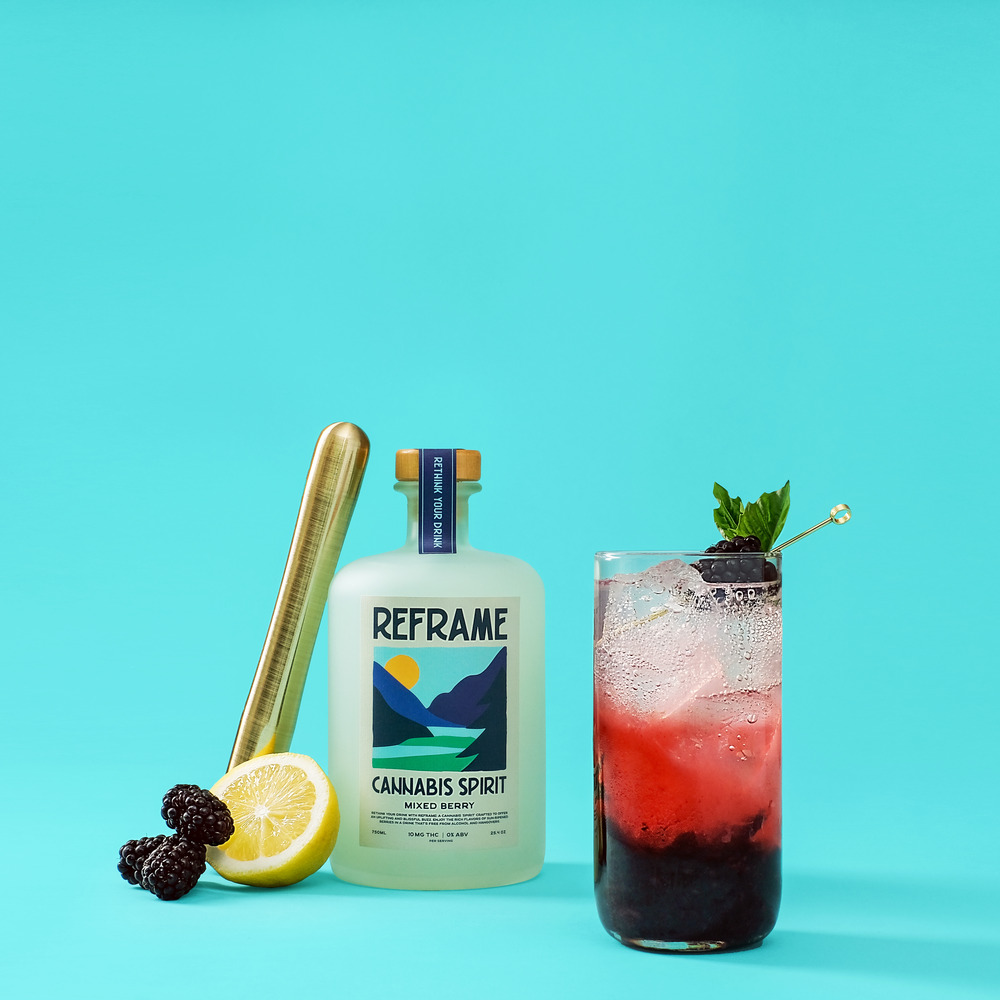 Bottle of Reframe cannabis spirit, cocktail, lemon, and blackberries on a blue background.
