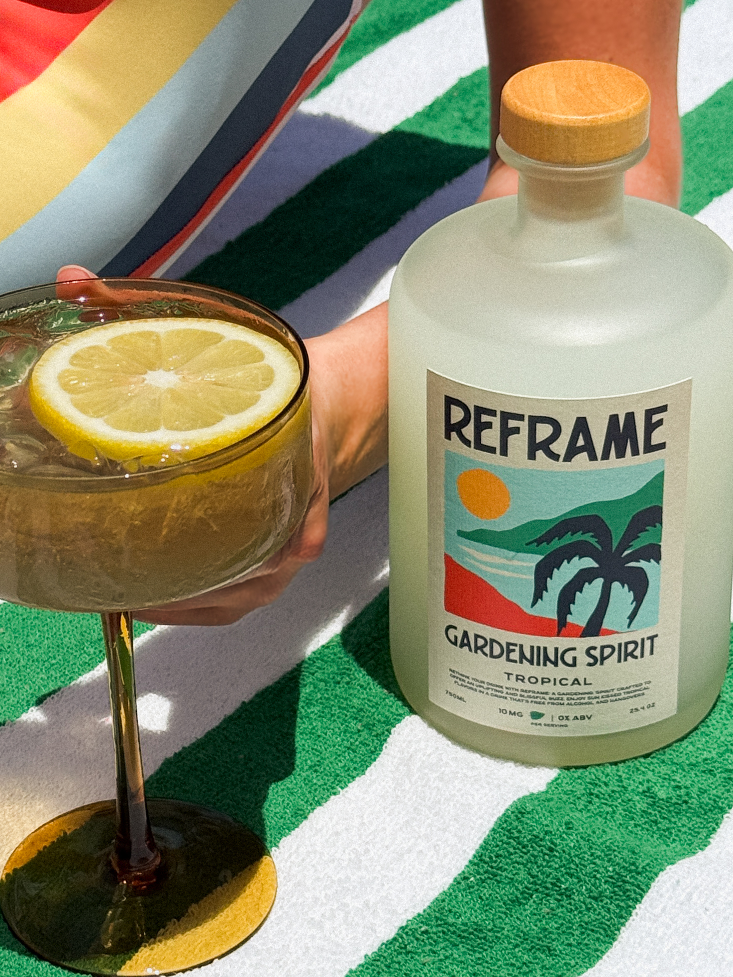 Bottle labeled 'Gardening Spirit' and a cocktail with a lemon slice on a striped towel.