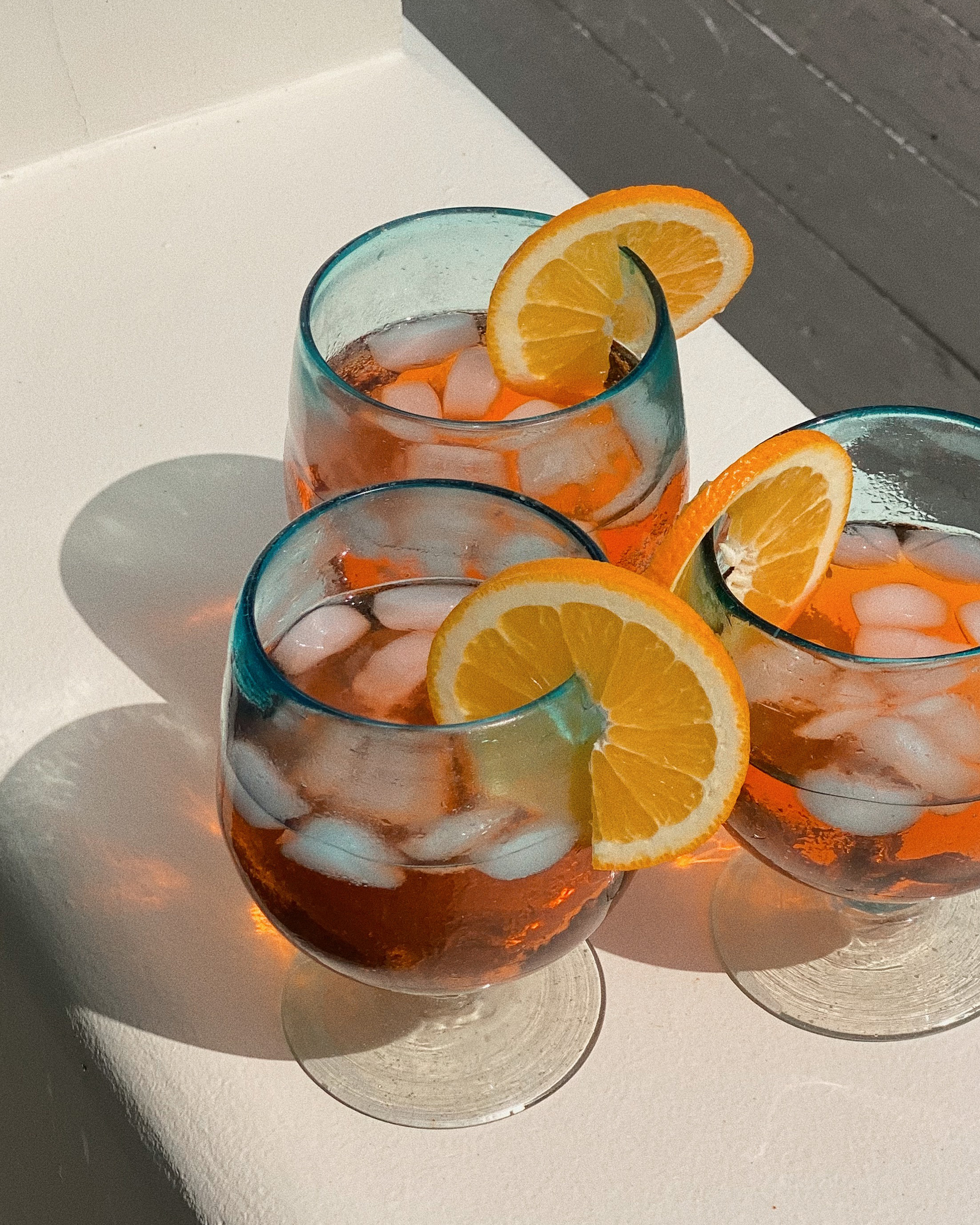 Three glasses of iced orange drinks with orange slices.