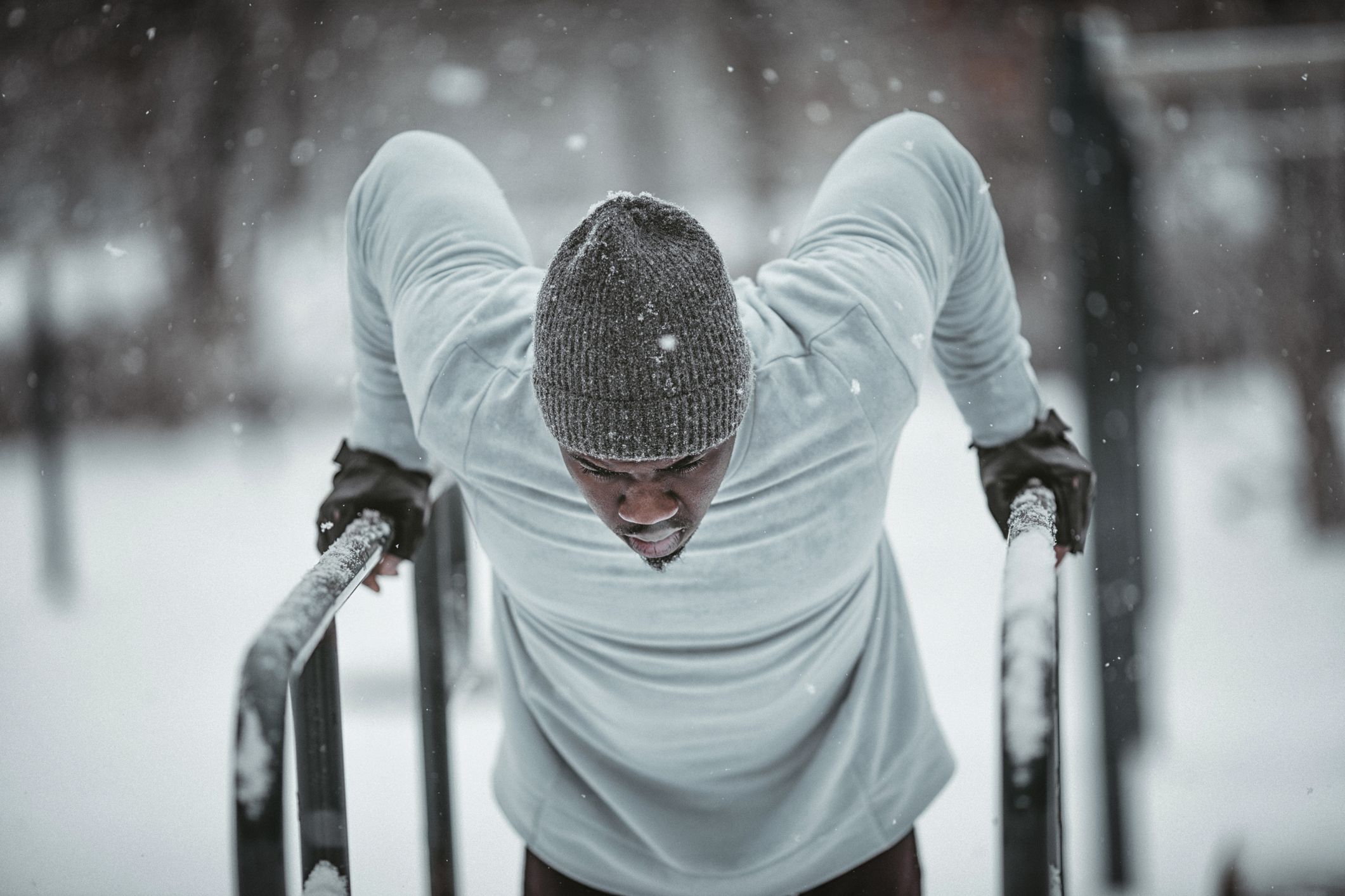 Person doing dips on parallel bars in the snow, wearing a beanie and gloves.