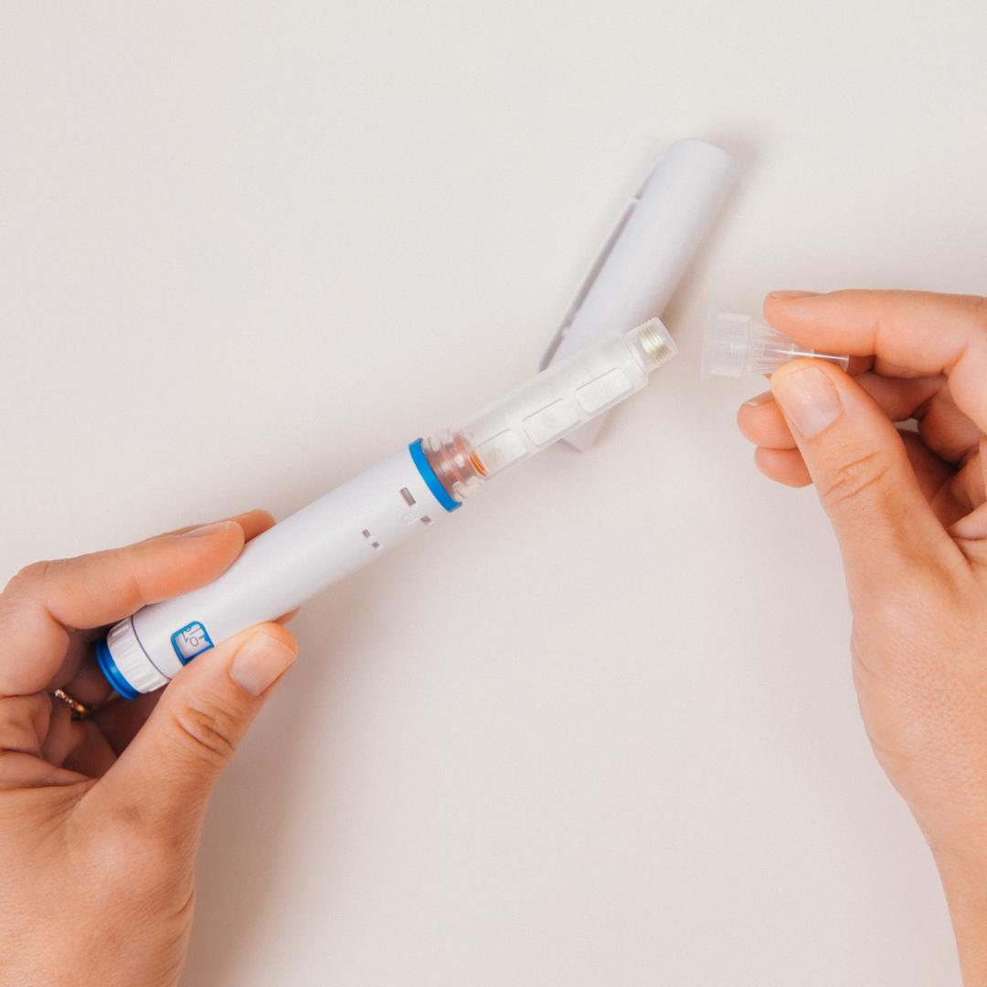 A person's hands attaching a needle to a medical injector pen against a plain white background.