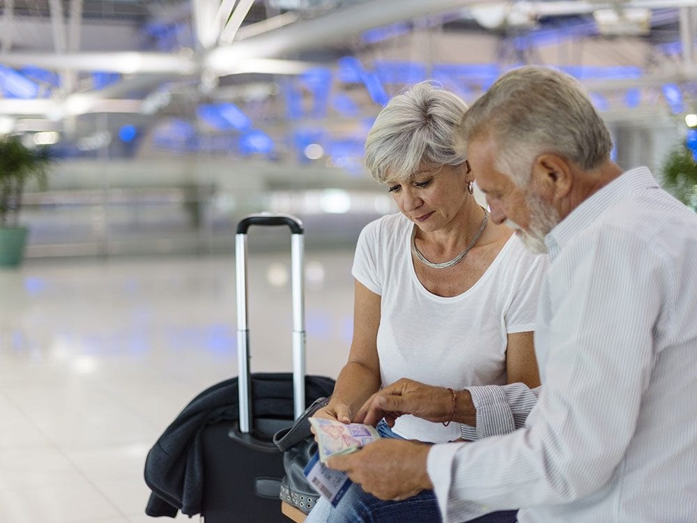 Two people sitting with luggage, looking at documents in an airport.