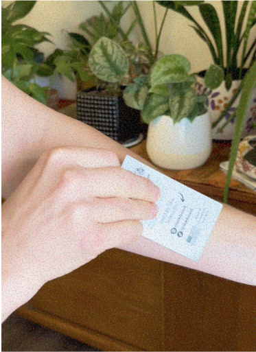 Person applying a patch to their arm, with plants in the background.