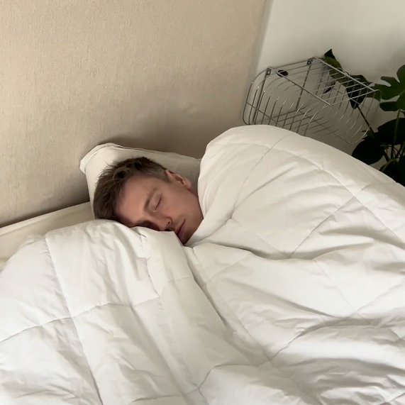 Person sleeping in bed under a white comforter.