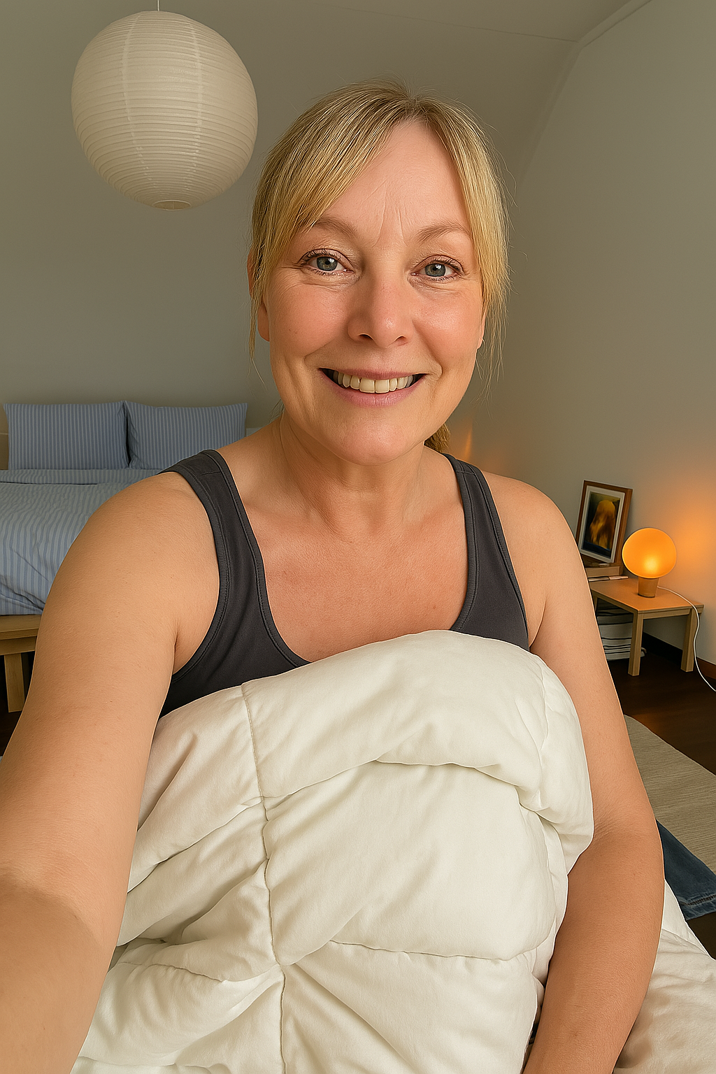 Smiling person holding a white blanket in a cozy bedroom.