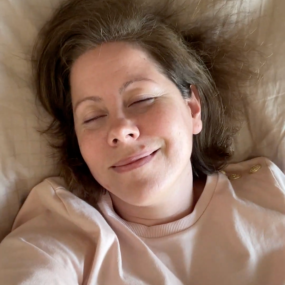 Person lying on a bed, smiling with eyes closed.