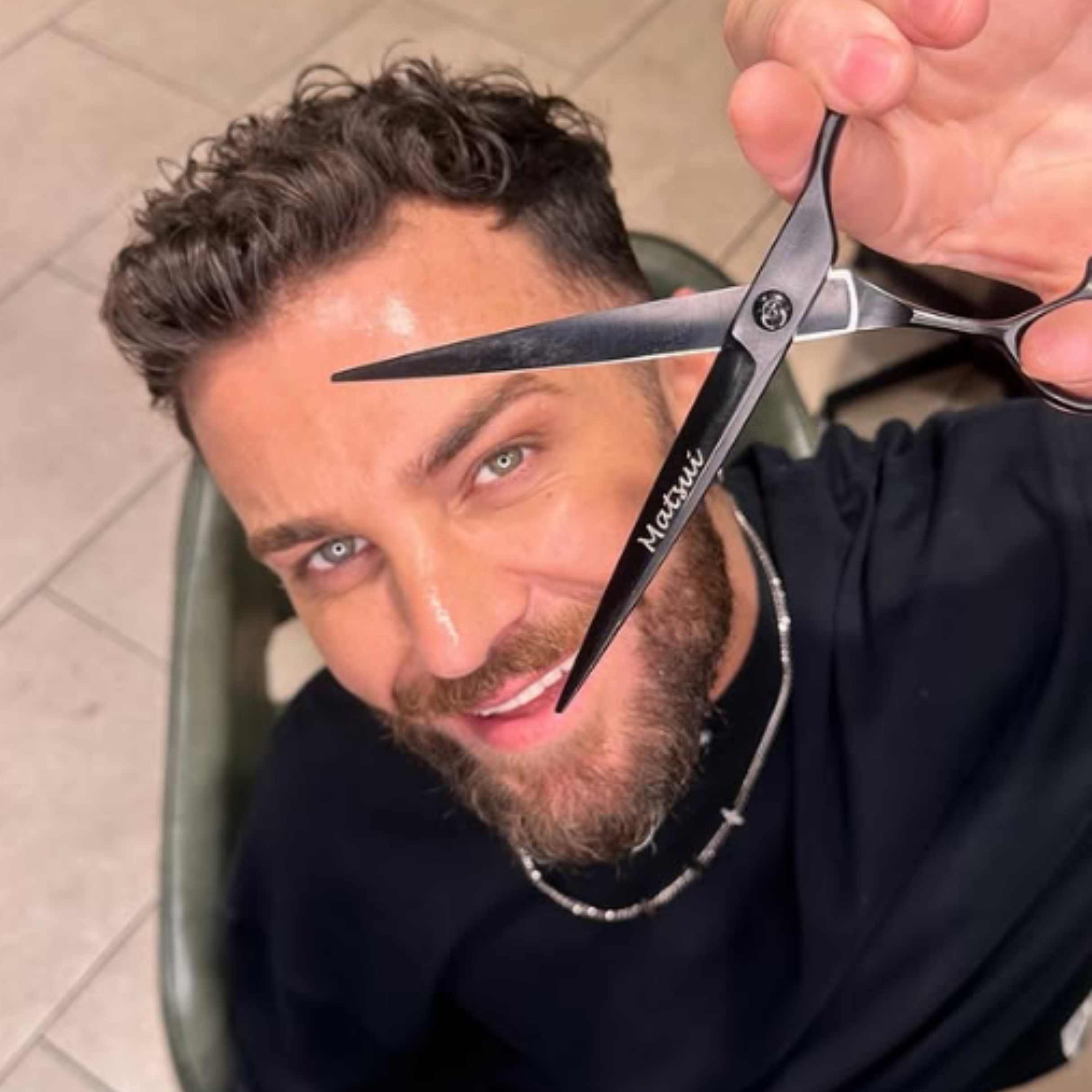 Man holding scissors, smiling, with curly hair and beard.