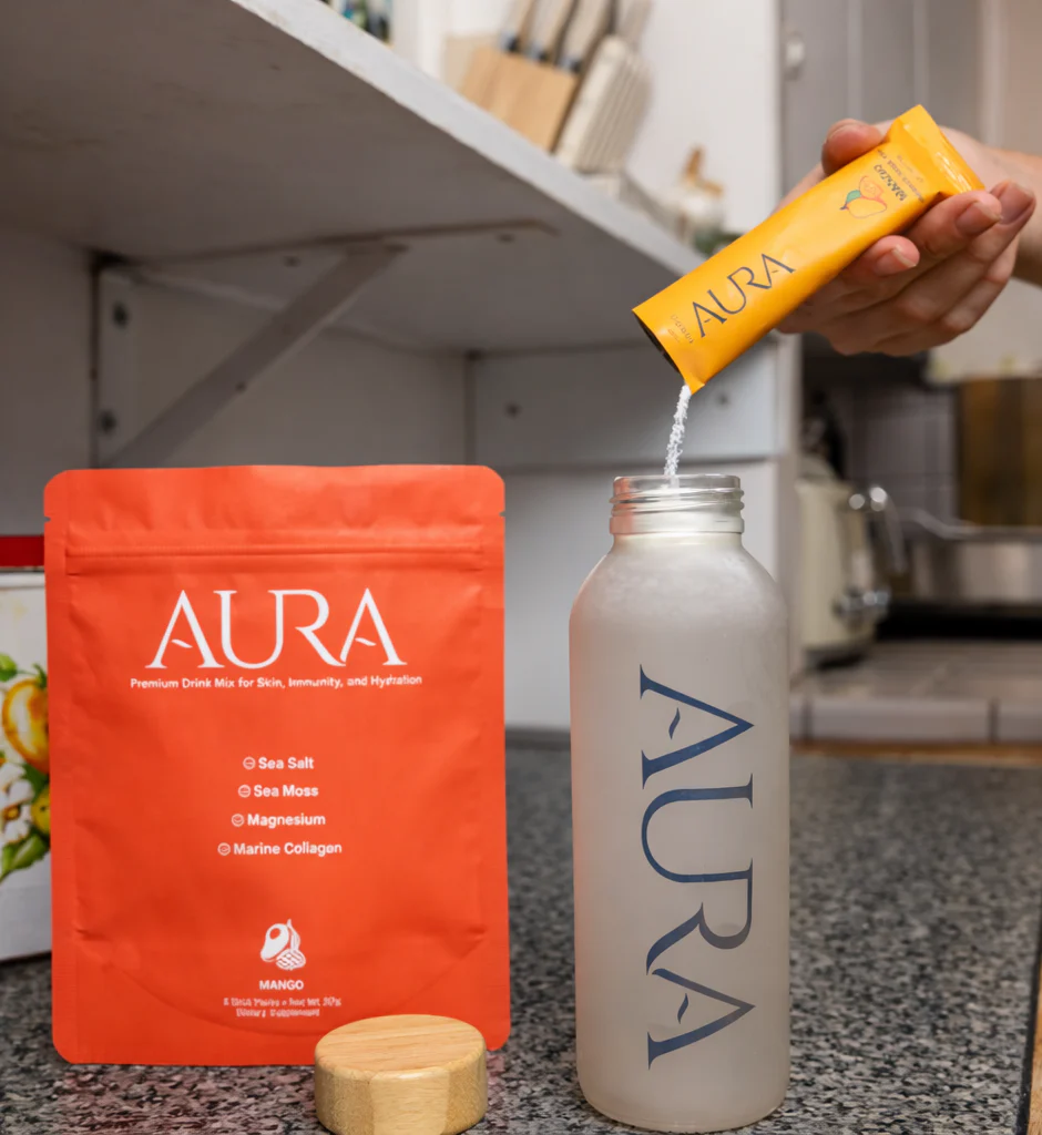 A hand pours Aura mango drink mix powder from a packet into a frosted water bottle.