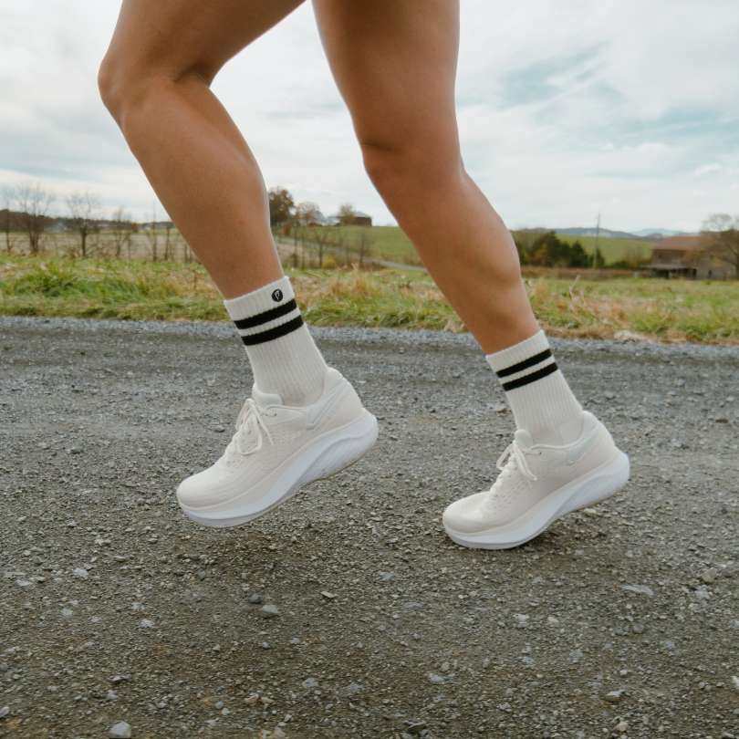Person running on gravel road wearing white sneakers and socks.