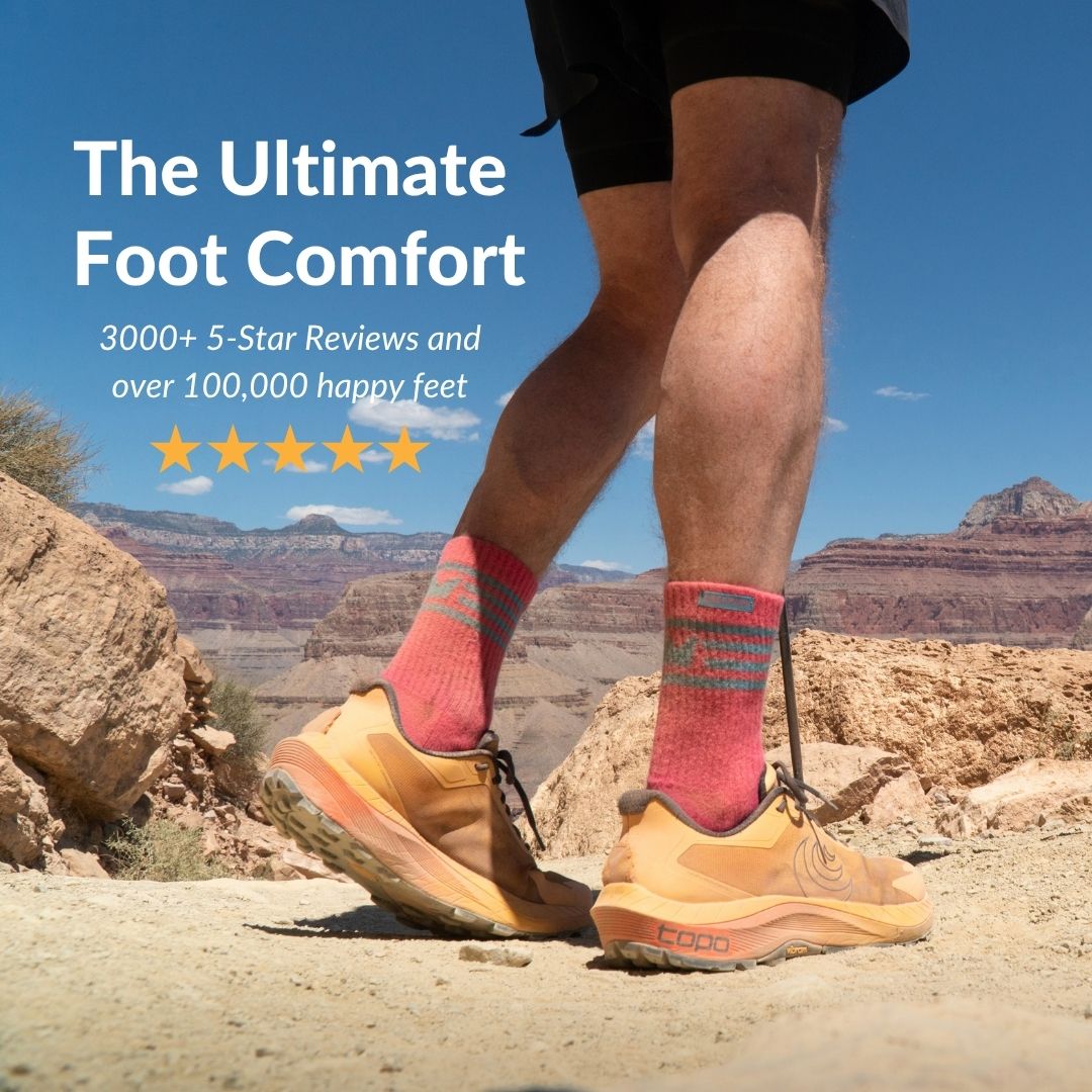 A low-angle shot of a person's legs wearing pink socks and trail shoes on a canyon path.