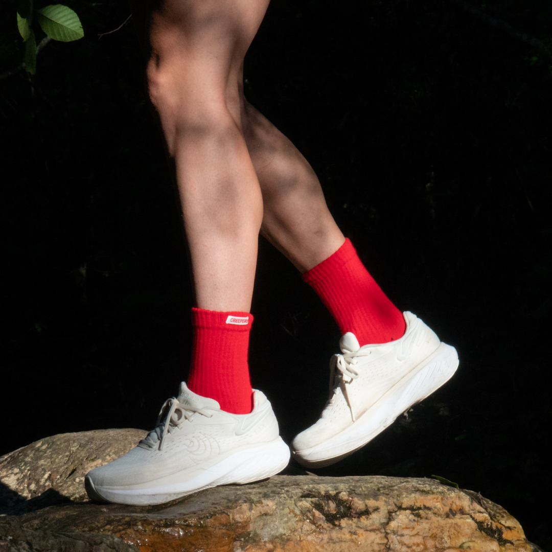A person wearing bright red socks and white sneakers stands on a rock in a dark setting.