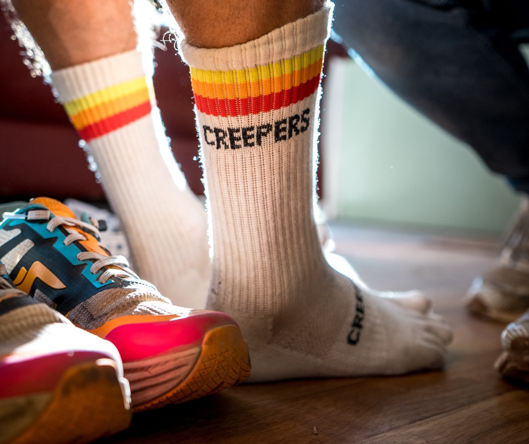 Person wearing white socks with 'CREEPERS' text, next to colorful running shoes.