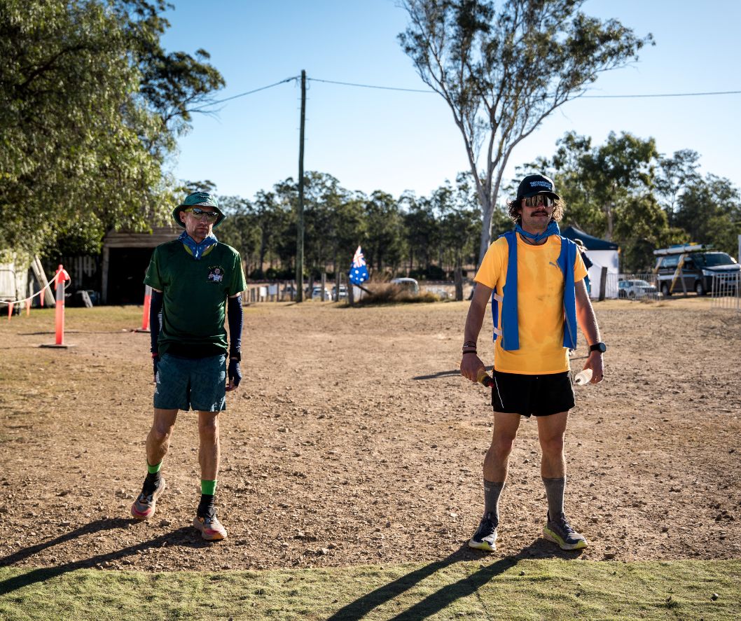 Two men in athletic gear standing outdoors on a sunny day.