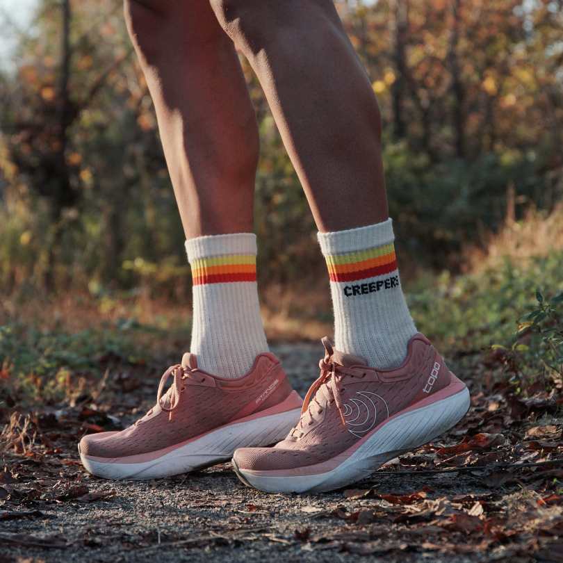 Person wearing pink sneakers and white socks standing on a forest path.
