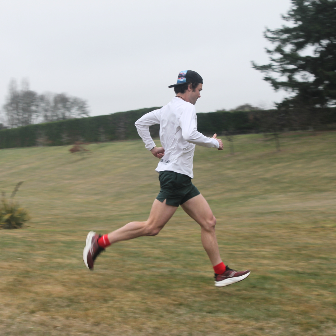 A man in a white long-sleeved shirt and a baseball cap runs across a grassy field.