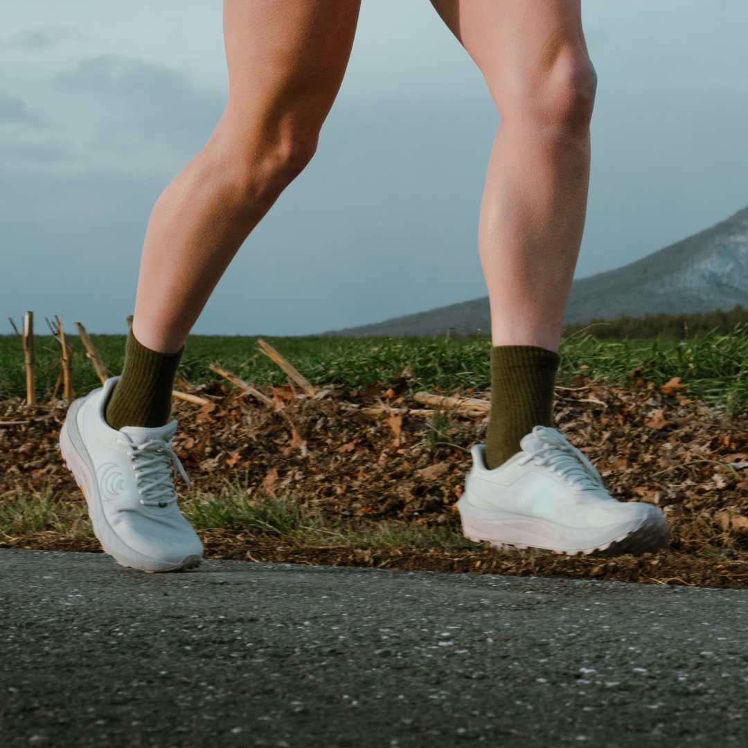 A runner's legs in purple 'CREEPERS' socks and light-colored shoes on a gravel road.