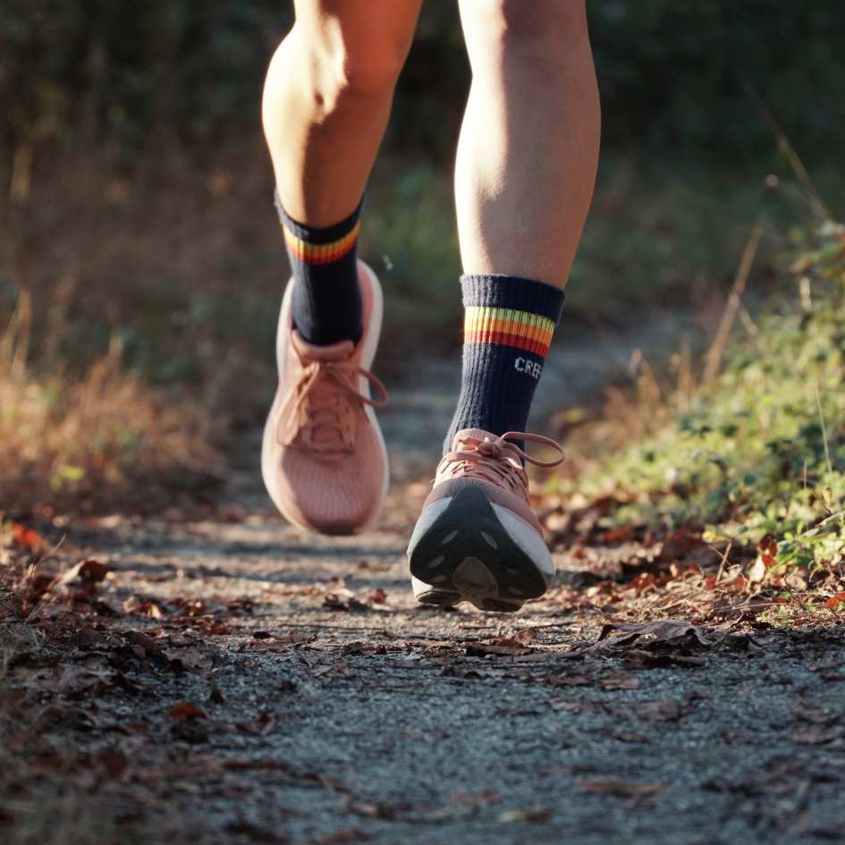 Person running on a wooded path, wearing pink shoes and striped socks.