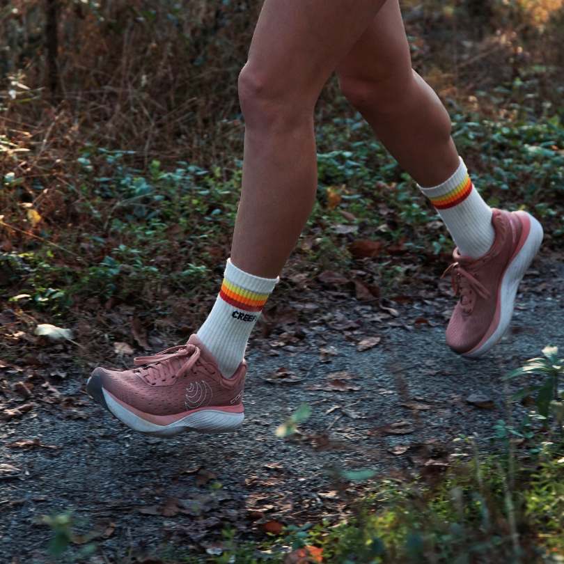Person walking on a trail wearing pink sneakers and striped socks.