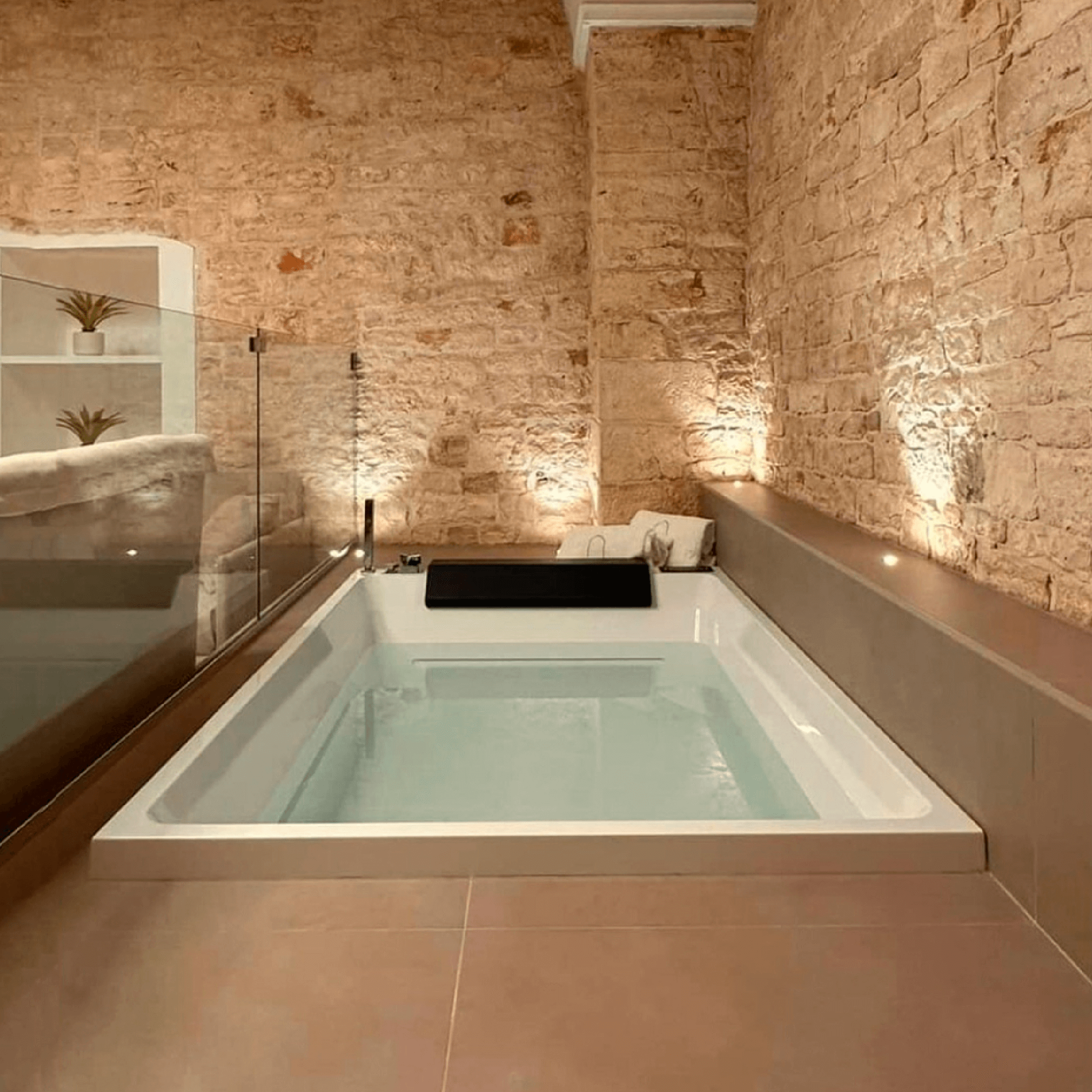 Modern recessed bathtub in a room with exposed brick walls and warm lighting.
